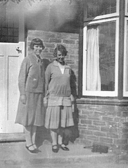 A couple of women standing outside a house
Description automatically generated