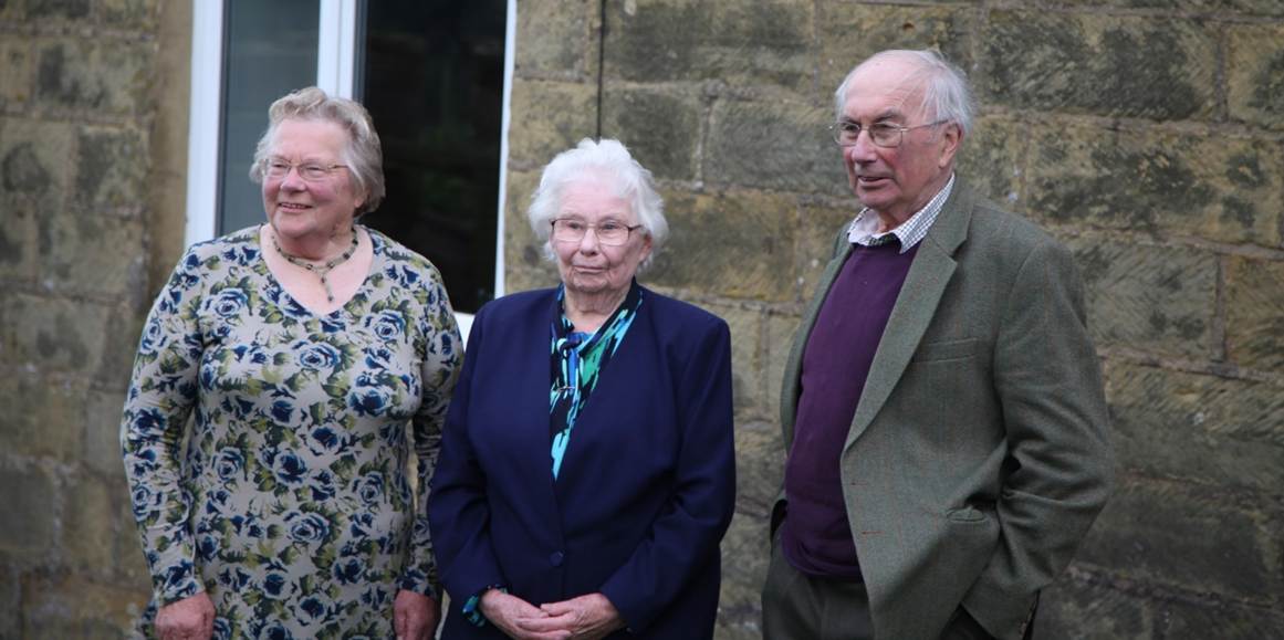 A group of old people standing outside a building
Description automatically generated