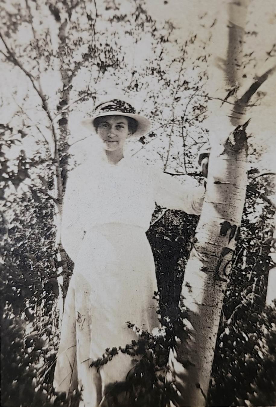 A person in a hat standing next to a tree
Description automatically generated
