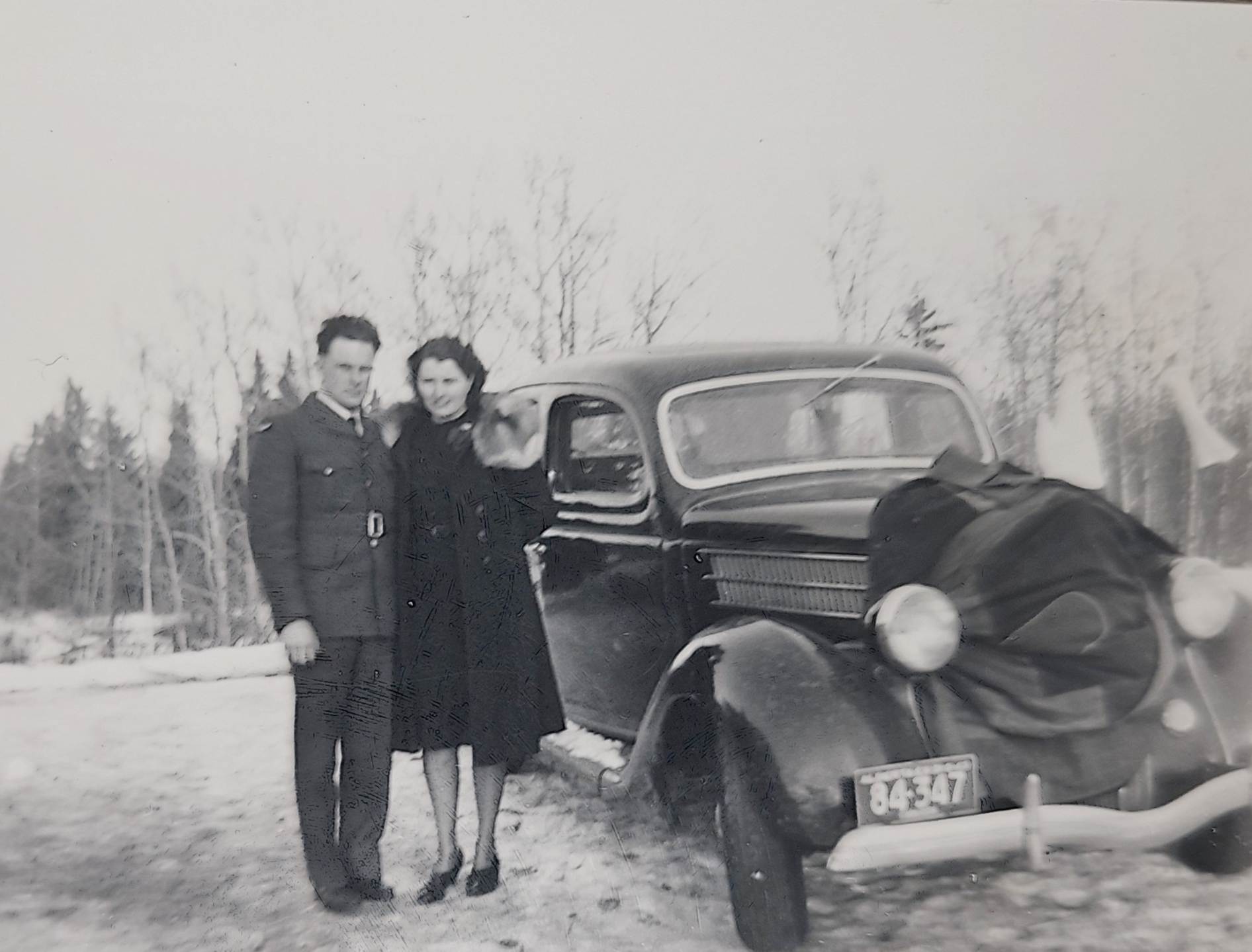 A person and person standing next to a car
Description automatically generated