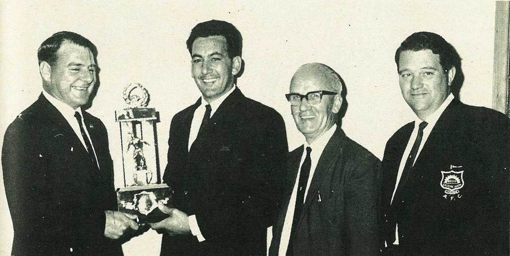 A group of men in suits holding a trophy
Description automatically generated