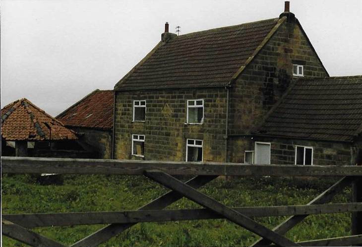 An old brick building with grass in front of a house
Description automatically generated