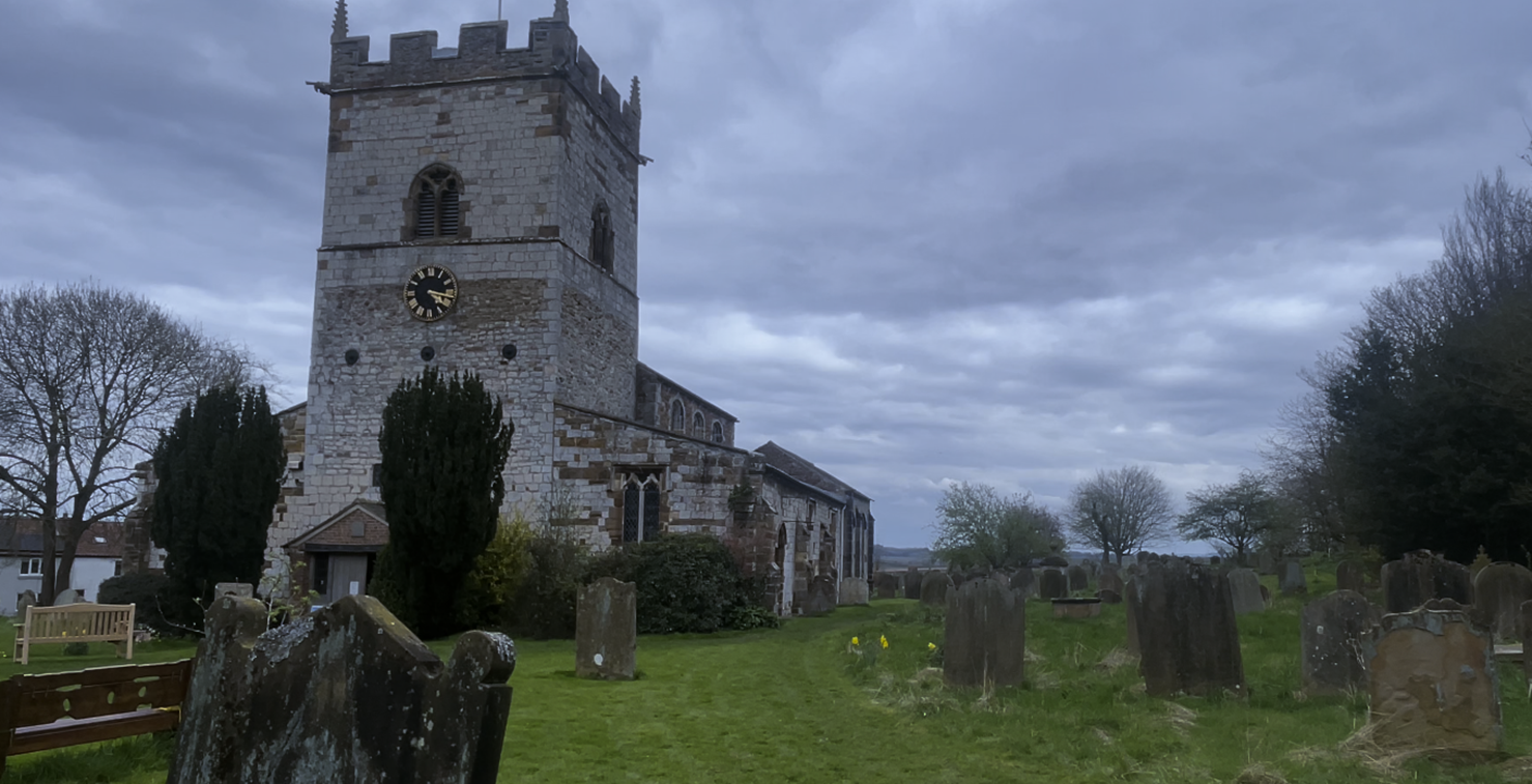 A stone building with a clock tower and a cemetery
Description automatically generated