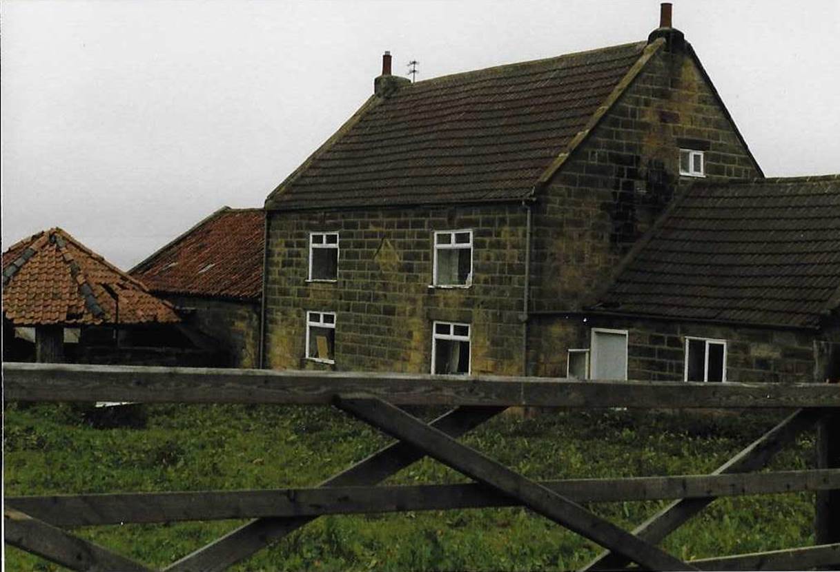 An old brick building with grass in front of a house
Description automatically generated