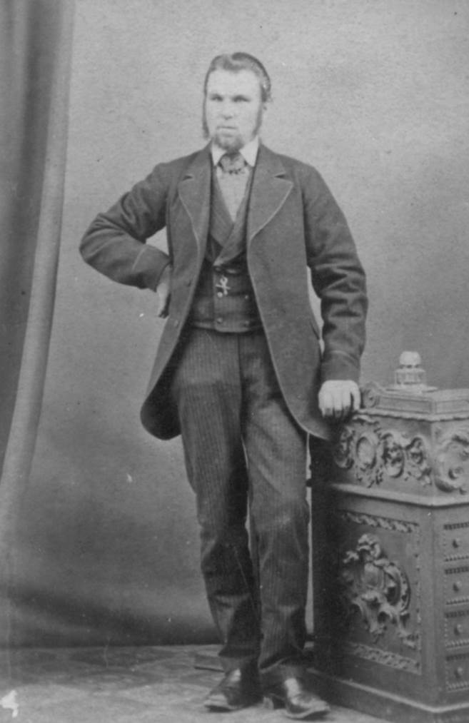 A person in a suit standing next to a chest
Description automatically generated