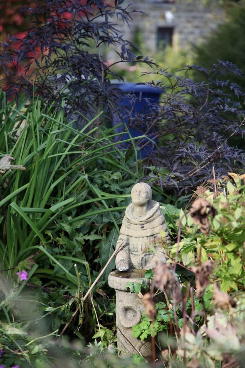 A small statue in a garden
Description automatically generated