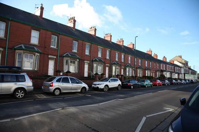 Long row of houses with cars parked on the side of the road
Description automatically generated